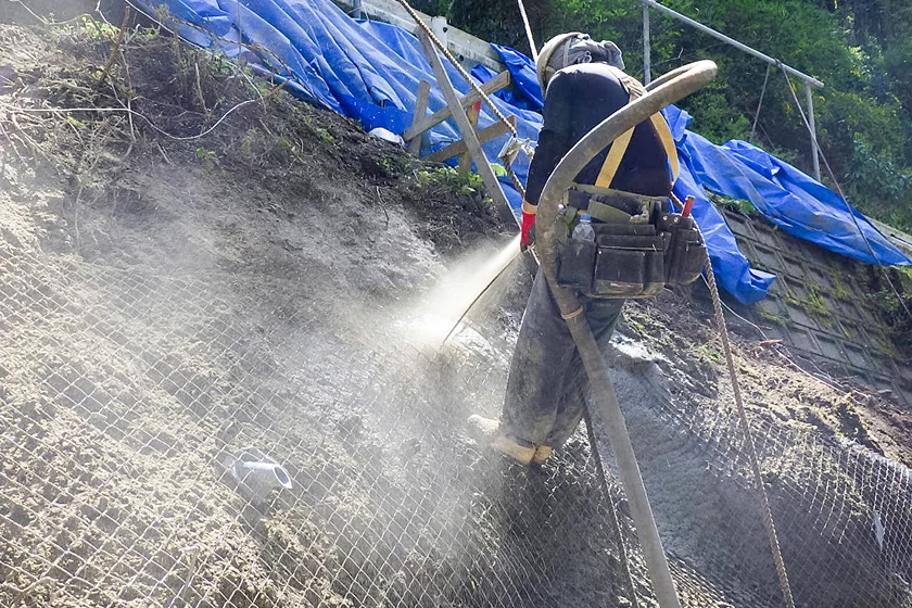 金網の上からモルタルを吹き付ける法面補強作業中の工事現場