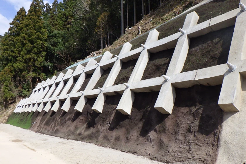 森林沿いの斜面に設置されたコンクリート格子補強とアンカーの施工後写真