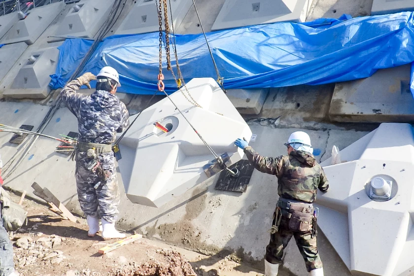 法面にコンクリートブロックを設置する作業員とクレーン作業の様子