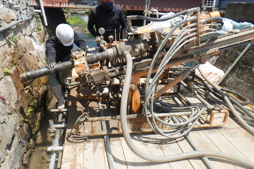 狭い現場で地盤に穴を開ける削孔機とそれを操作する作業者