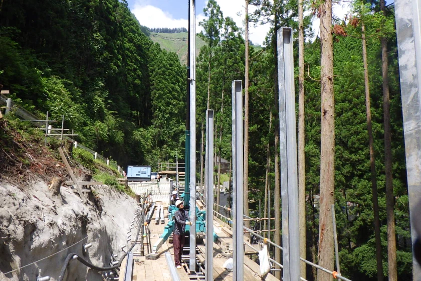 法面沿いに鋼製支柱を立てる落石対策工事中の現場